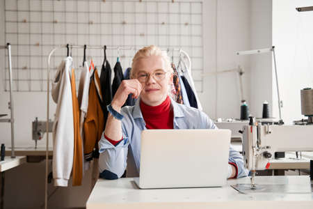 Man wearing glasses looking to the camera while working at his laptop computer