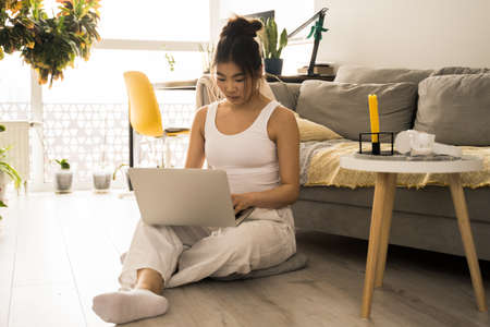 Girl freelancer sitting at the floor while working at computer from home