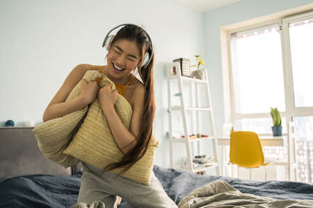 Girl dancing with the pillows at the bed and enjoying of the listening music