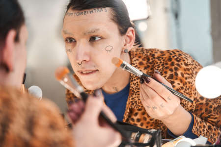 Man sitting in front of the mirror and applying foundation on his face