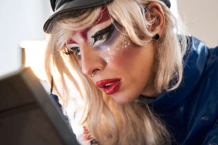 Drag queen with creative makeup looking at himself while painting lipsの写真素材