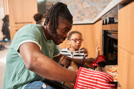 Parent and his multiracial daughters smiling while standing in kitchenの写真素材