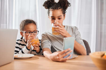 Sisters watching cartoons at the smartphone while having breakfast