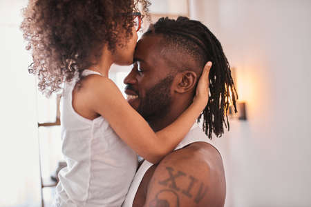 Daughter smiling, kissing at the forehead her father and hugging himの写真素材