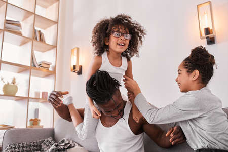 Father and his daughters obsessed while playing at the sofaの写真素材