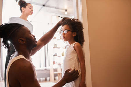 Man with dreadlocks measuring height of his curly little daughterの写真素材