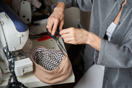 Tailor sewing handmade hat in her workshop, while sitting at the sewing machineの写真素材