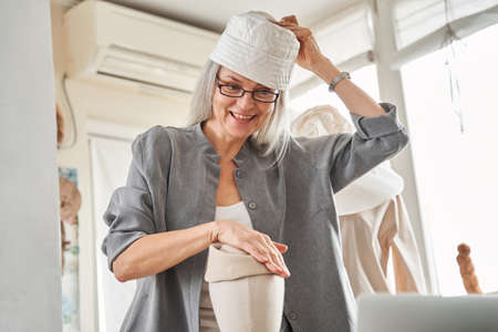 Woman looking at the laptop screen with happy smile while trying on her hat