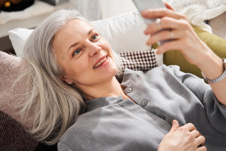 Smiling mature woman at home using modern smartphoneの写真素材