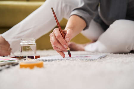 Woman holding brush while painting at home with watercolorsの写真素材