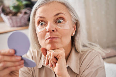 Woman with under eye patches looking at the mirror with funny faceの写真素材