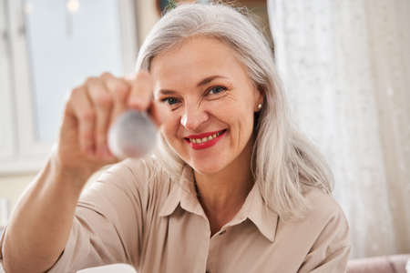 Woman showing makeup brush to the camera while sitting at the bed