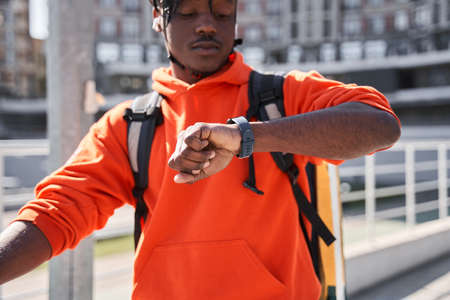 Delivery courier man sitting at the bicycle and looking at his smartwatch