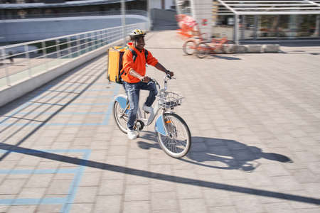 Delivery man wearing red sweatshirt and yellow delivery backpack sitting at the bicycleの写真素材