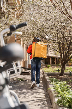 Courier with yellow backpack looking for a way to the client while delivering orders