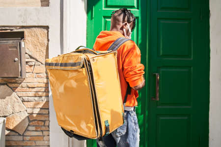 Courier standing is under the door and holding big yellow bag with foodの写真素材