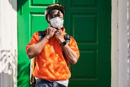 Man wearing helmet, protective mask and delivery backpack standing near clients door