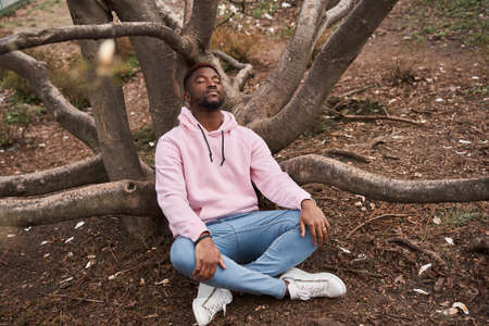 Man sitting cross-legged near the tree, practicing yoga and enjoying meditationの写真素材