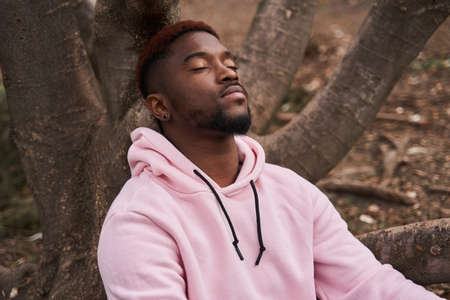 Man wearing casual sweatshirt sitting near the tree at the forest or parkの写真素材
