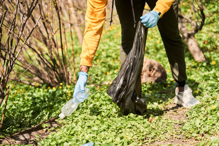 Man wearing casual clothes and gloves with trash bag in hands cleaning forest