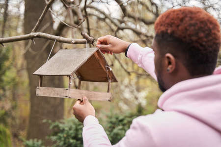Man adjusting birds feeder at the tree and preparing to the feeding birds