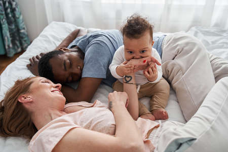 Multiracial parents and cute small kids lying on bed togetherの写真素材