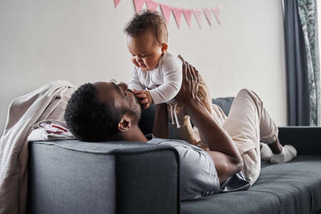 Daddy laying with his baby on the sofa, looking at the son with love and care