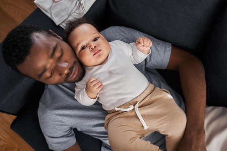 Father laying with his little baby on the sofa and relaxing