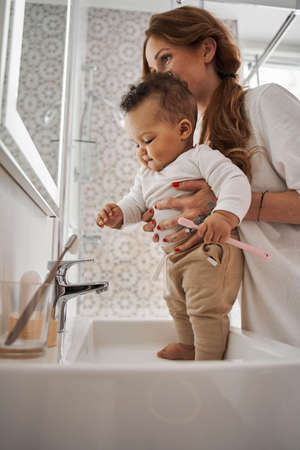 Girl stretching her hands to the water while her mother holding her at the handsの写真素材