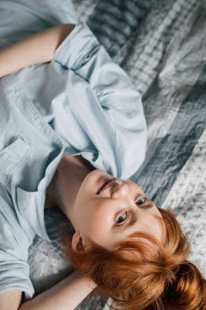 Woman looking at the camera and laying at the back at the bedの写真素材