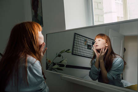 Woman looking at herself at the mirror, touch her face and feeling satisfied