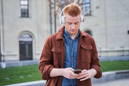 Man looking at the smartphone and listening music while standing