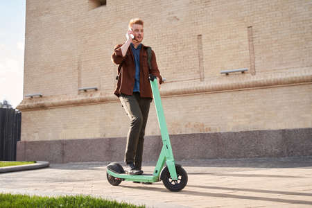 Male riding powered ecological transport and having conversation at the mobile phoneの写真素材