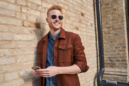Man wearing sunglasses standing near the brick wall and looking away