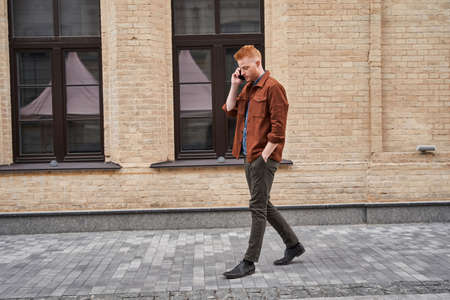 Man walking through the urban street and chatting with somebody using smartphoneの写真素材