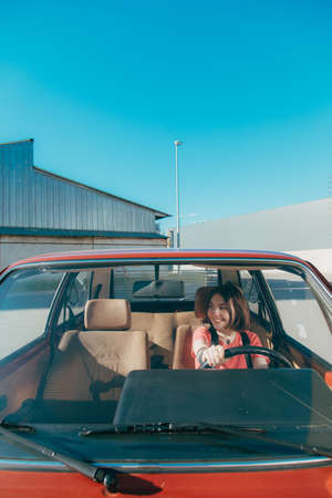 Woman in car indoor keeps wheel and turning around while smiling looking at the windowの写真素材