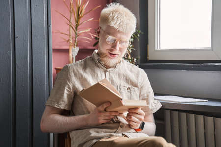 Man wearing glasses sitting at the lonely room and reading a bookの写真素材