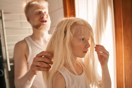 Girl standing at the bathroom and waiting while her father making braids for herの写真素材