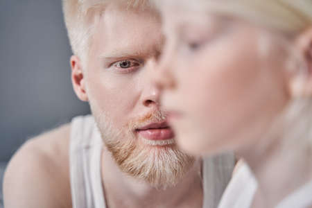 Man looking attentively to the camera while sitting near his blonde daughterの写真素材