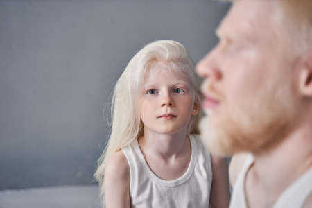 Girl sitting near her father and looking attentively to the camera while posing