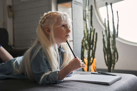 Girl laying at the sofa and pondering while drawing at the paper
