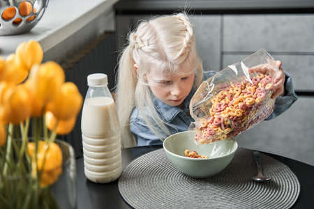 Girl pouring corn flakes into the plate while preparing breakfast