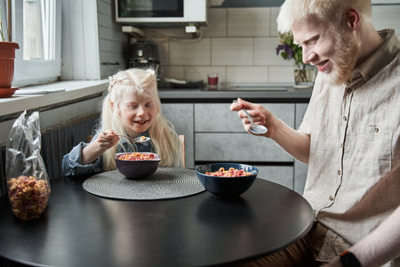 Albino family of father and daughter eating corn flakes with milk at the breakfast