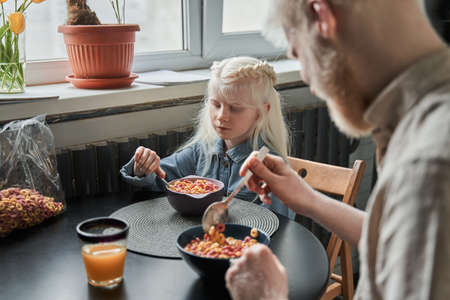 Father sitting at the table with his blonde daughter and preparing eating corn flakes