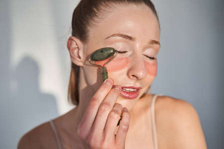 Girl with vitiligo skin applying patches under eyes with massage rollerの写真素材