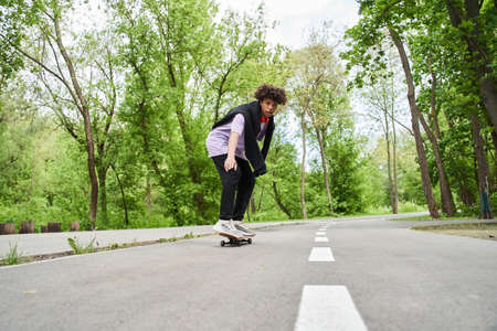 Man with curly hair performing with skateboard on a road at the summer street