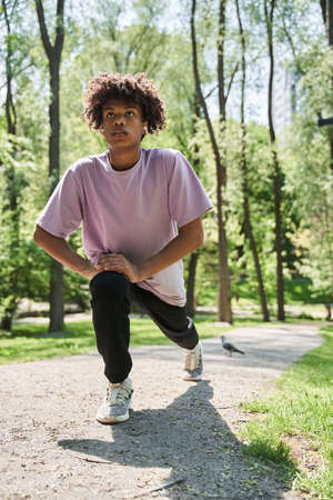 Teenager warming up before a morning workout at the park at the morning around the trees