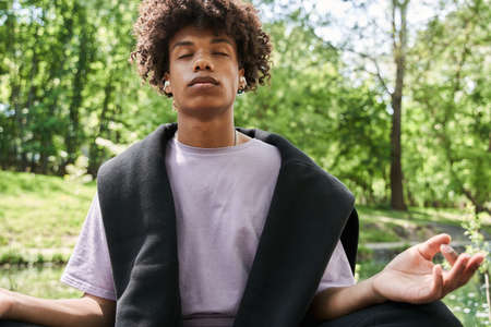 Man keeping eyes closed and meditating at the cozy forest or park