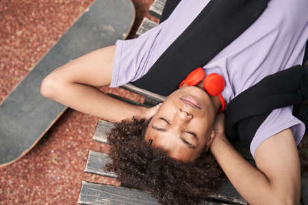 Guy laying at the bench with closed eyes and relaxing after riding at the skateboardの写真素材