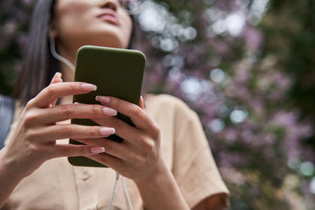 Female listening music while situating at the street and holding her smartphoneの写真素材